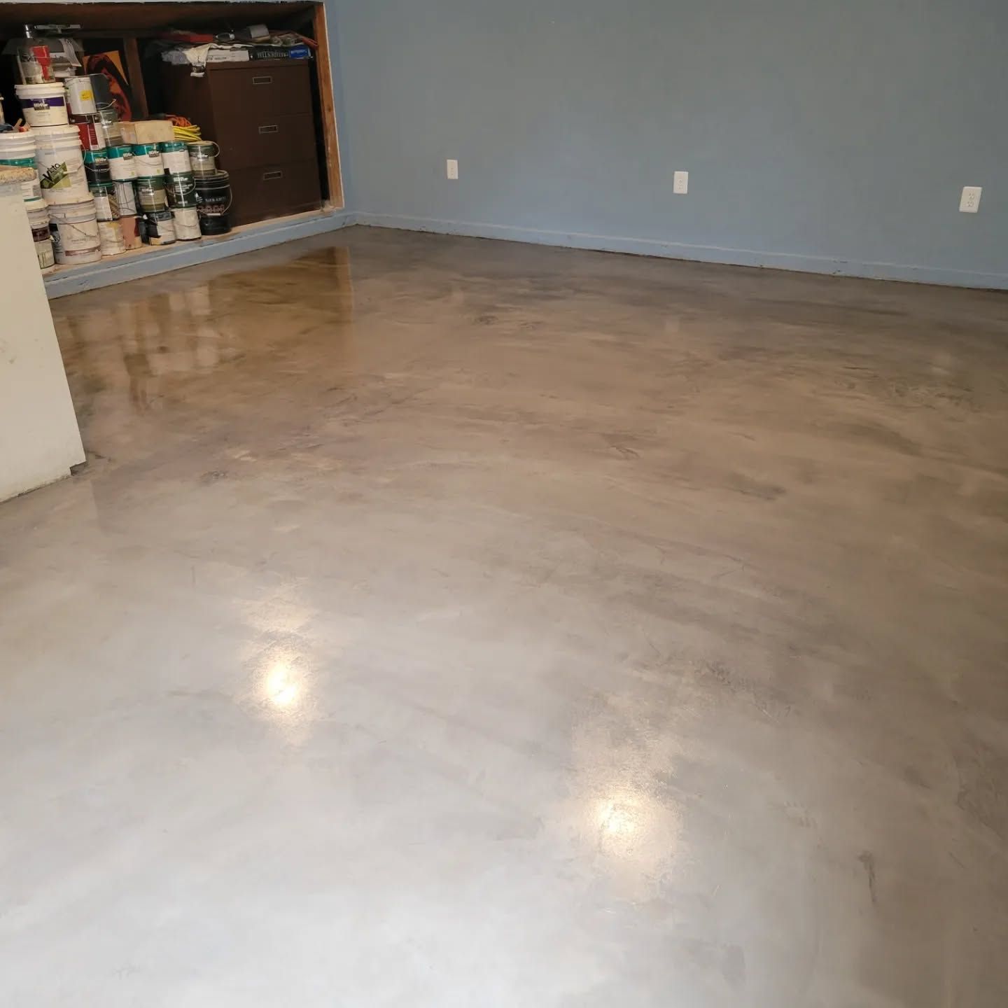 A room with a polished concrete floor, blue walls, and storage shelves filled with paint cans.