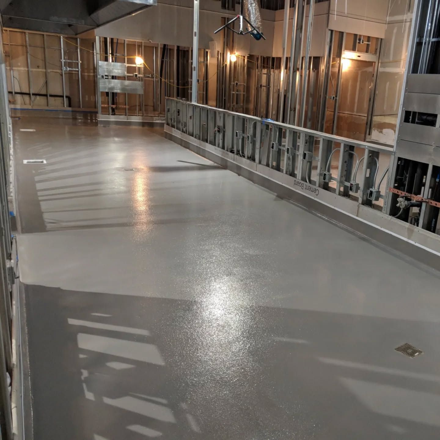 Interior construction site with gray concrete floor, metal studs, and open walls.