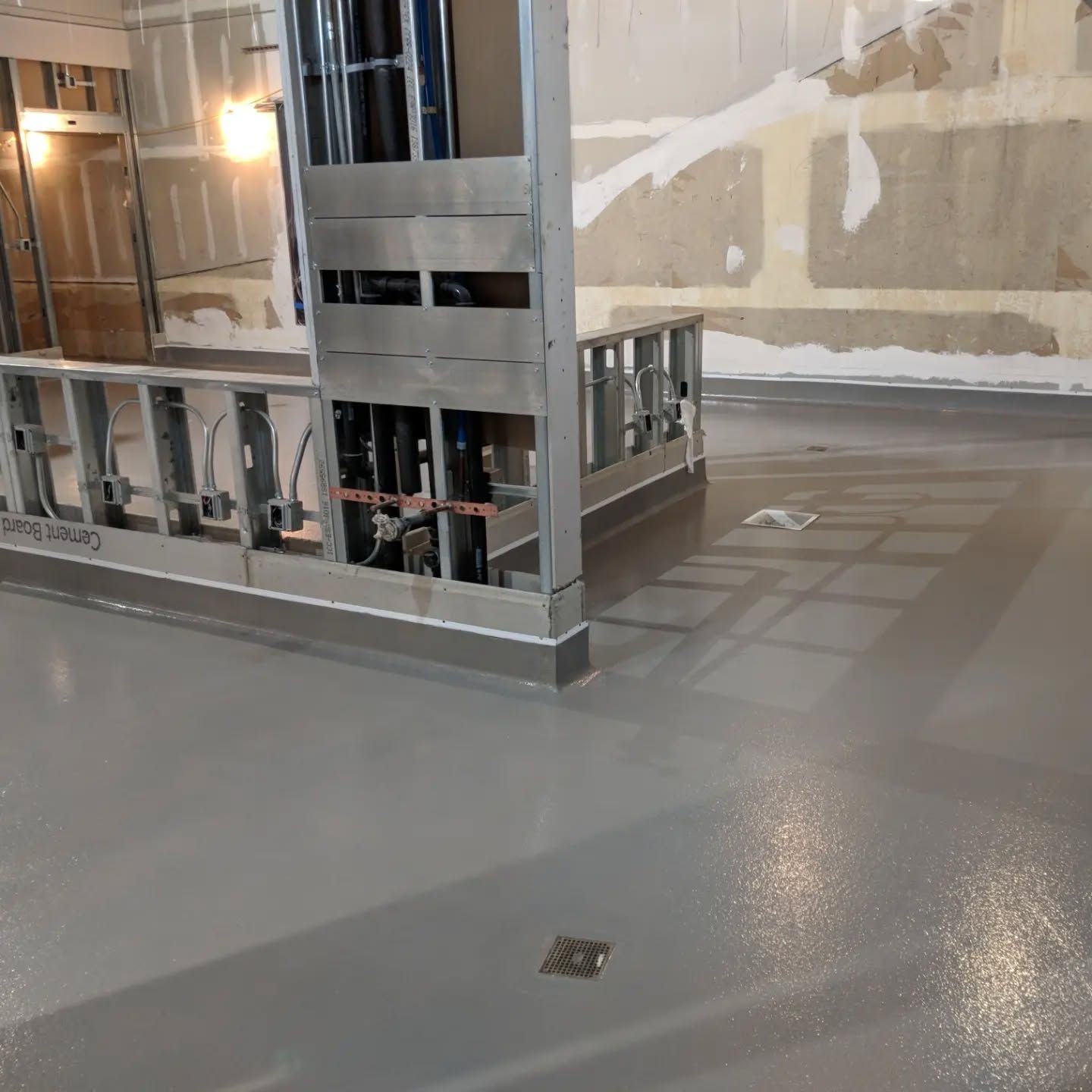 Construction site with gray flooring, metal framing, and exposed pipes.