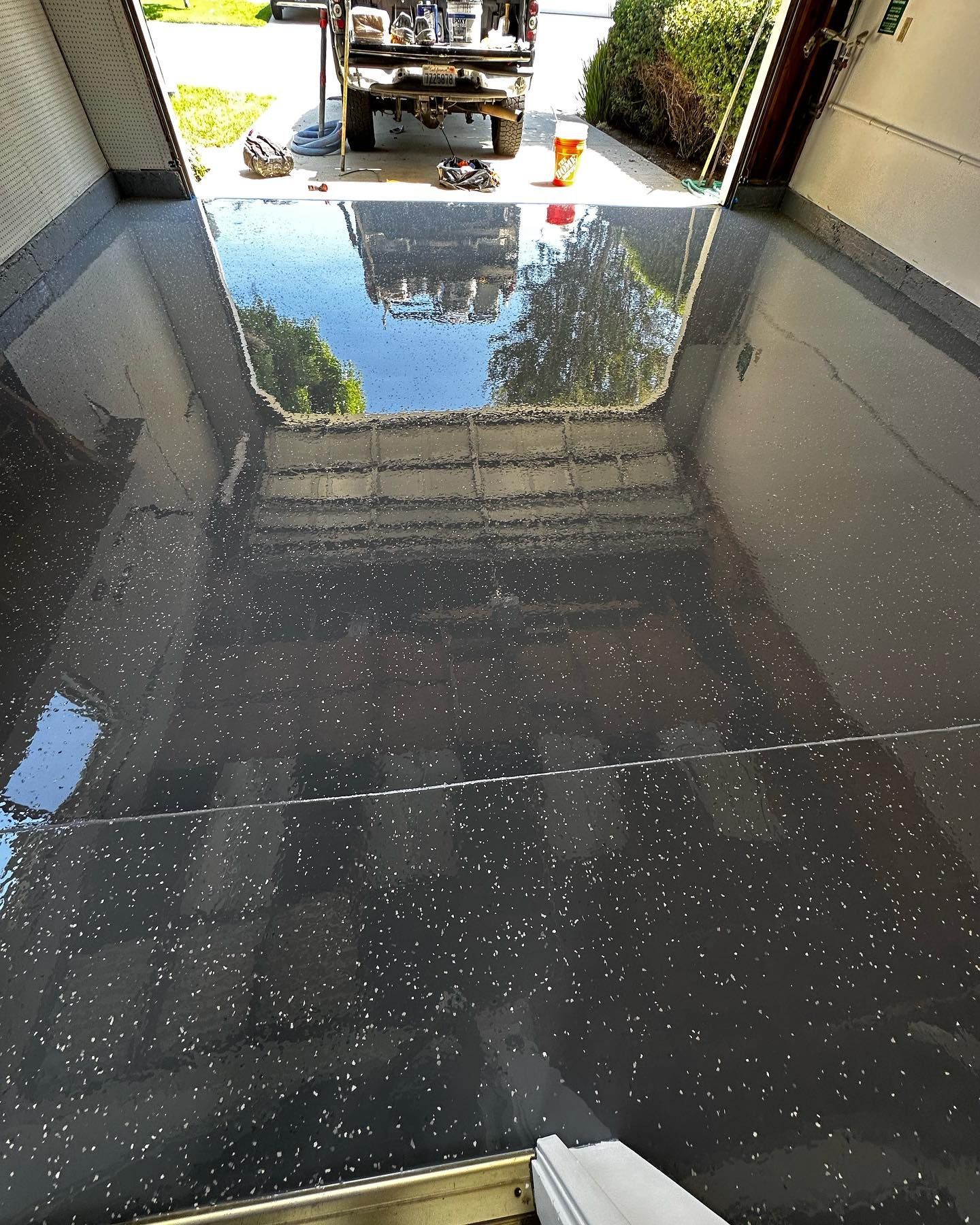 Dark gray epoxy garage floor with reflective flecks. Garage door open, showing the sky and a vehicle outside.