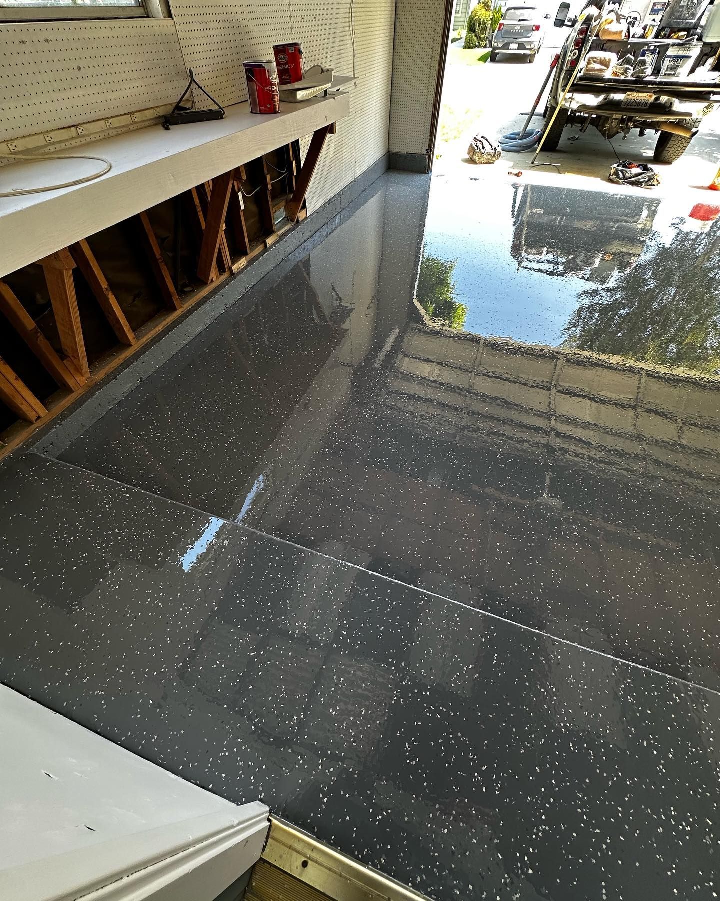 Garage with gray speckled epoxy floor and open doorway to a sunny street.