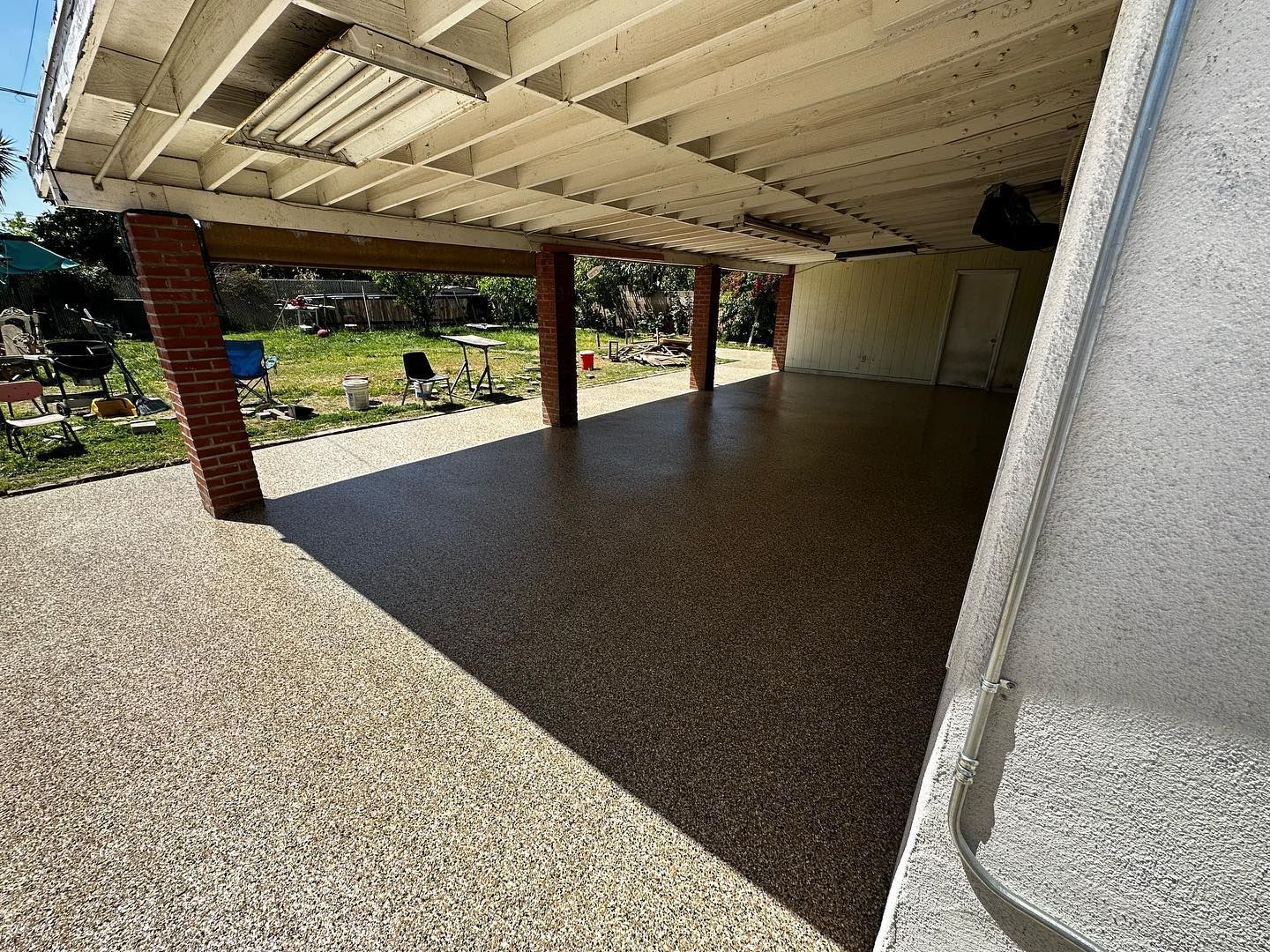 Covered patio with speckled flooring, brick columns, and a view of a backyard.