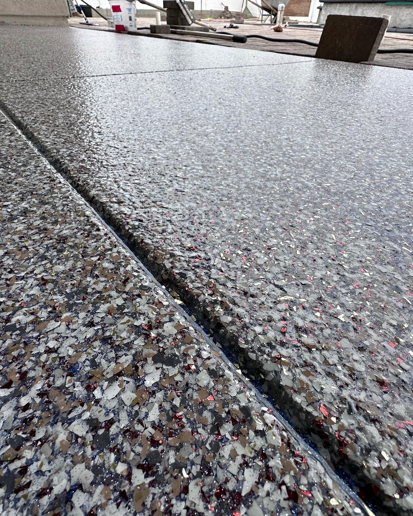 Close-up of a speckled floor with a prominent seam; dark gray and red flakes are visible.