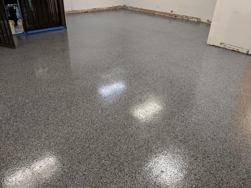 Gray epoxy-coated floor in a room, reflecting light. The walls are white and the door frame is black.