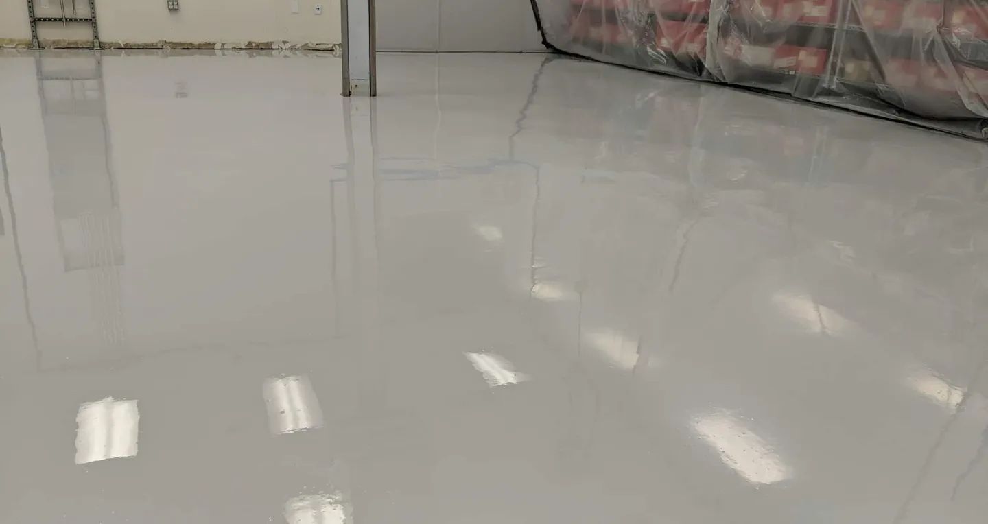 White epoxy floor inside a warehouse, reflecting overhead lights and a partially visible storage unit.
