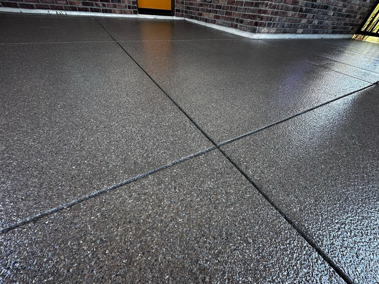 Textured concrete surface with intersecting dark lines, near a brick wall and door.