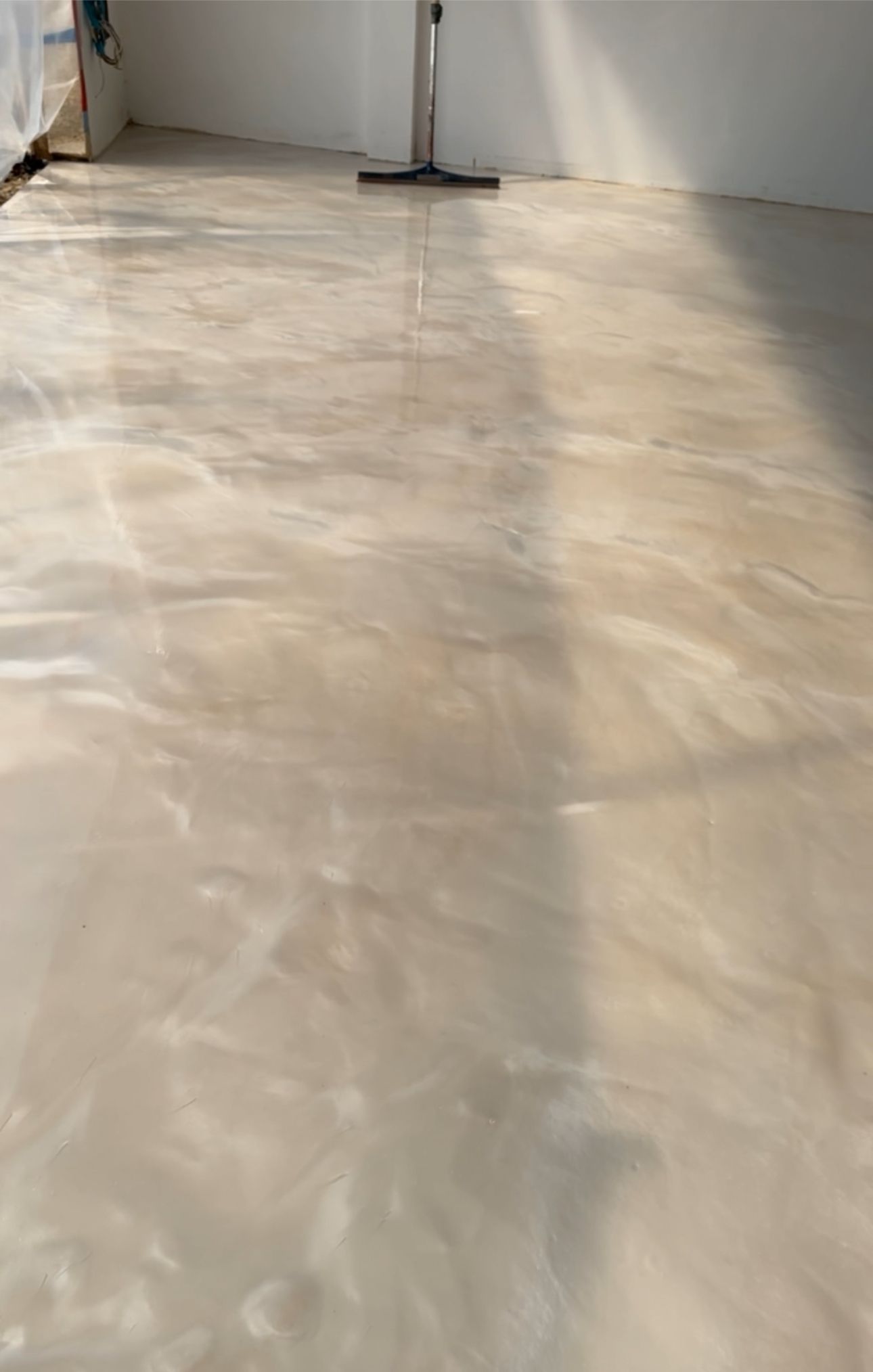 Shimmering, light-toned epoxy flooring with swirled patterns and a vacuum cleaner in the background.