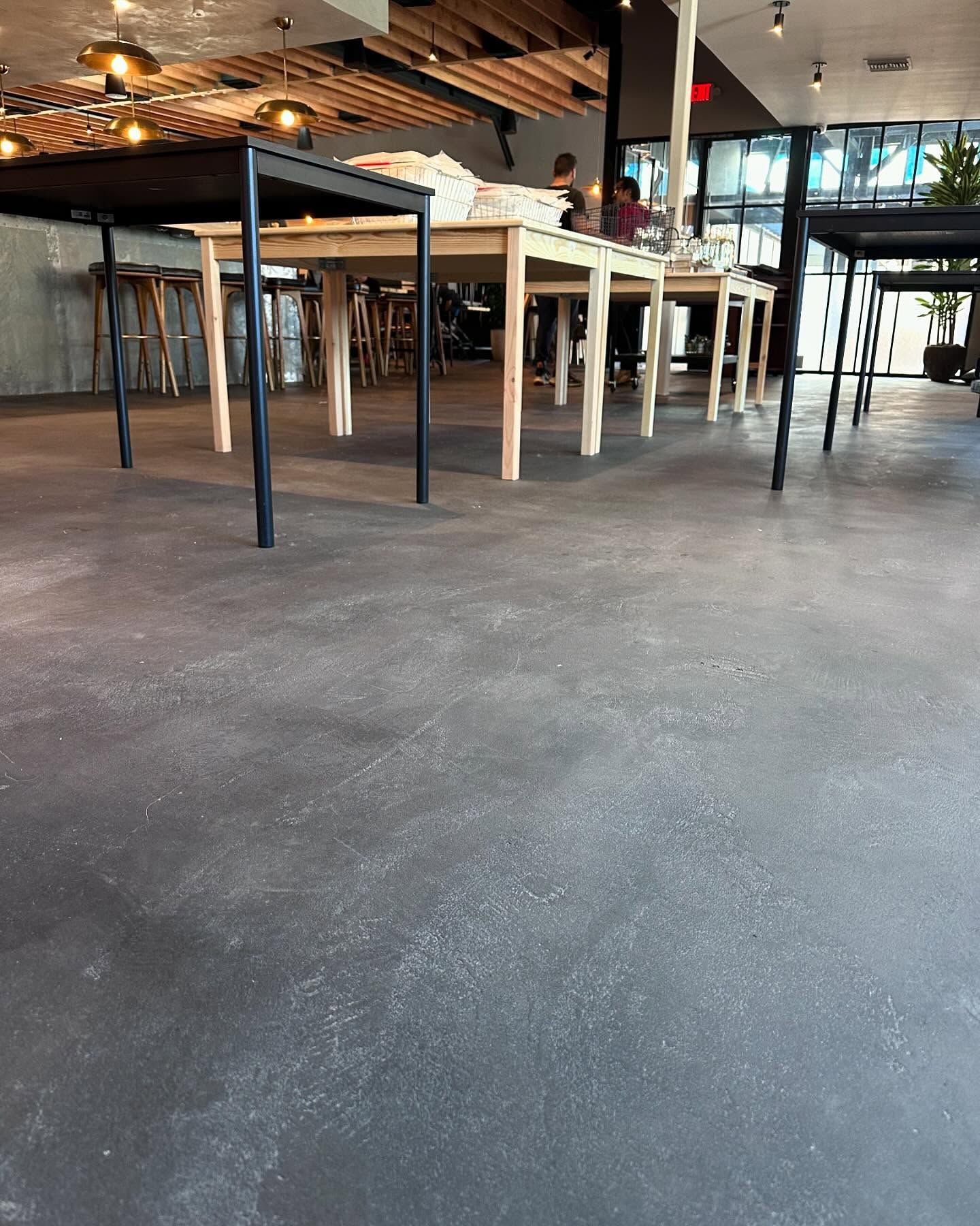 Gray concrete floor in a commercial space, tables with light-colored wood legs, and overhead lighting.