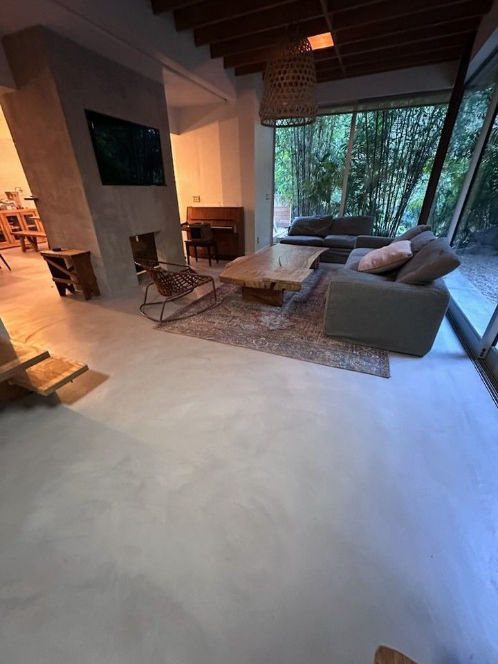 Living room with modern design, concrete floor, large windows with a view to trees.