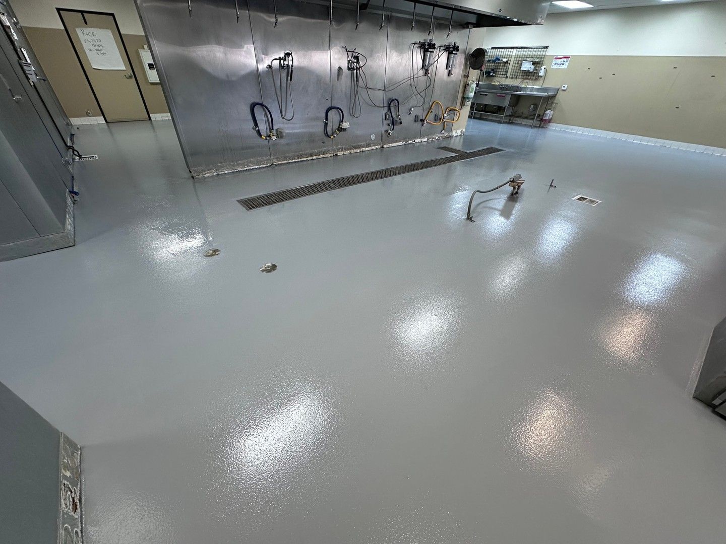 Grey, glossy floor in a commercial kitchen with stainless steel equipment and a drain in the floor.