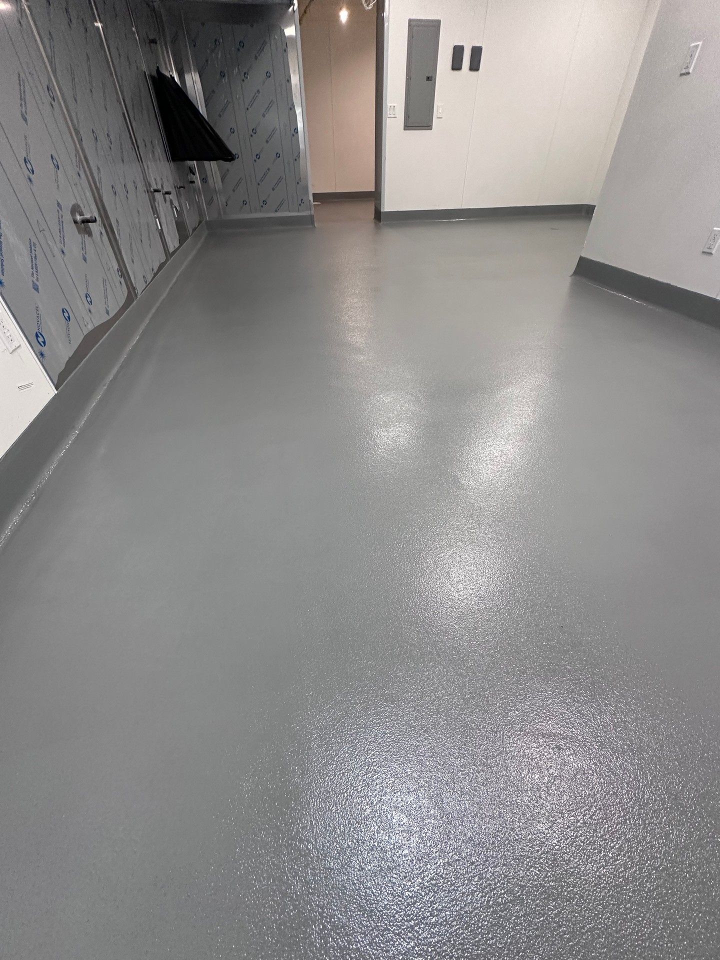 Gray floor with a slightly glossy finish in a hallway with white walls and a door at the end.