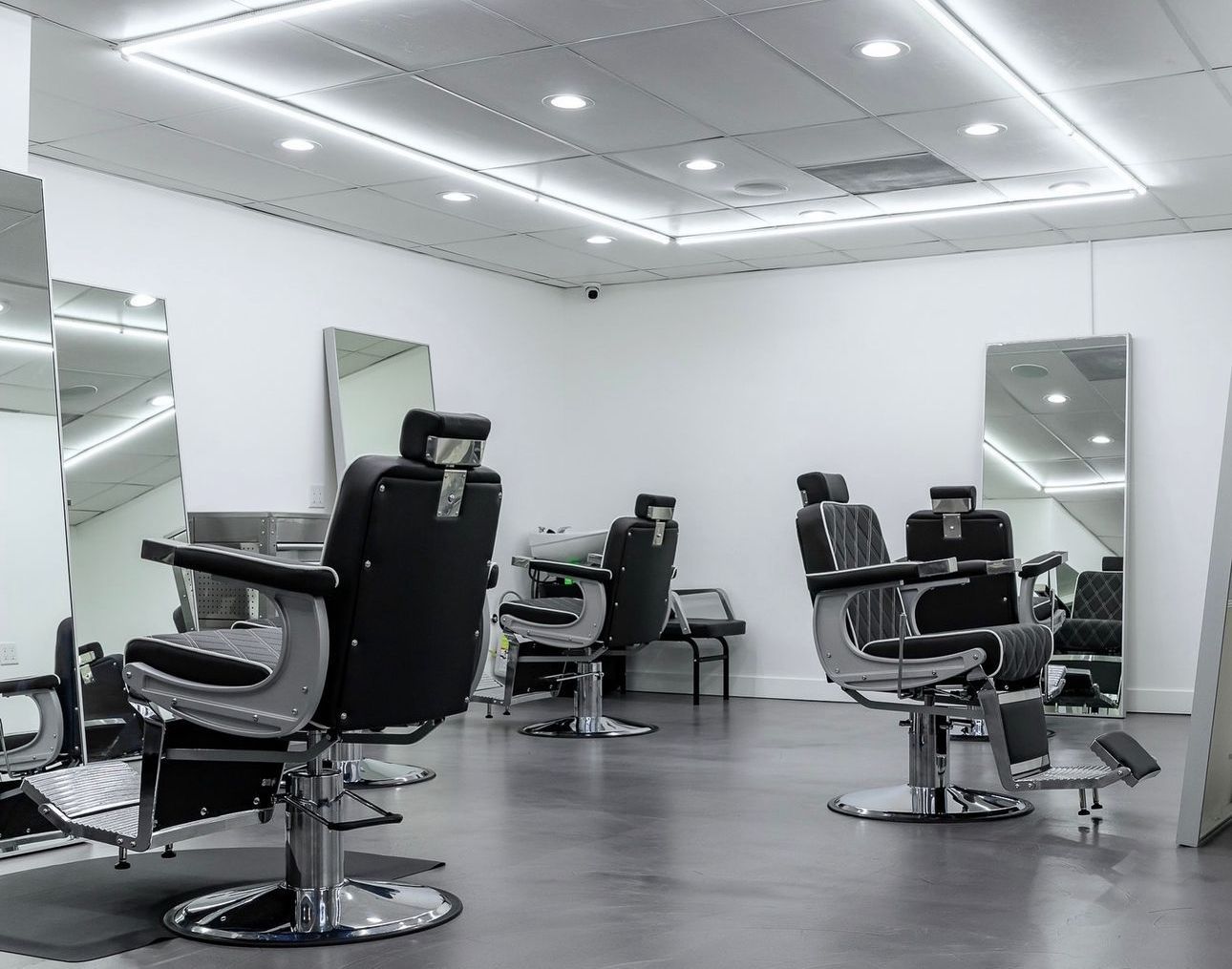 Barber shop interior with black barber chairs, large mirrors, and recessed lighting.