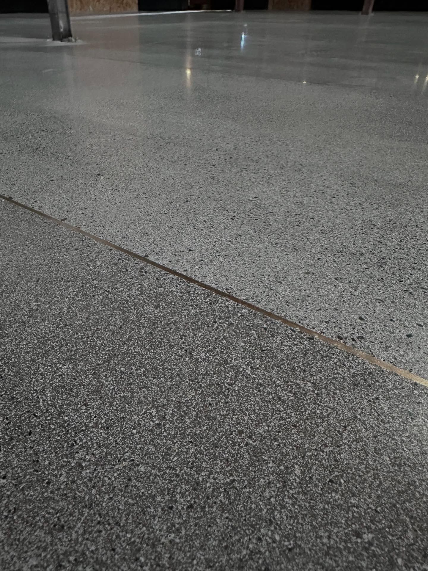 Polished concrete floor, divided by a thin brass strip, with a column in the background.