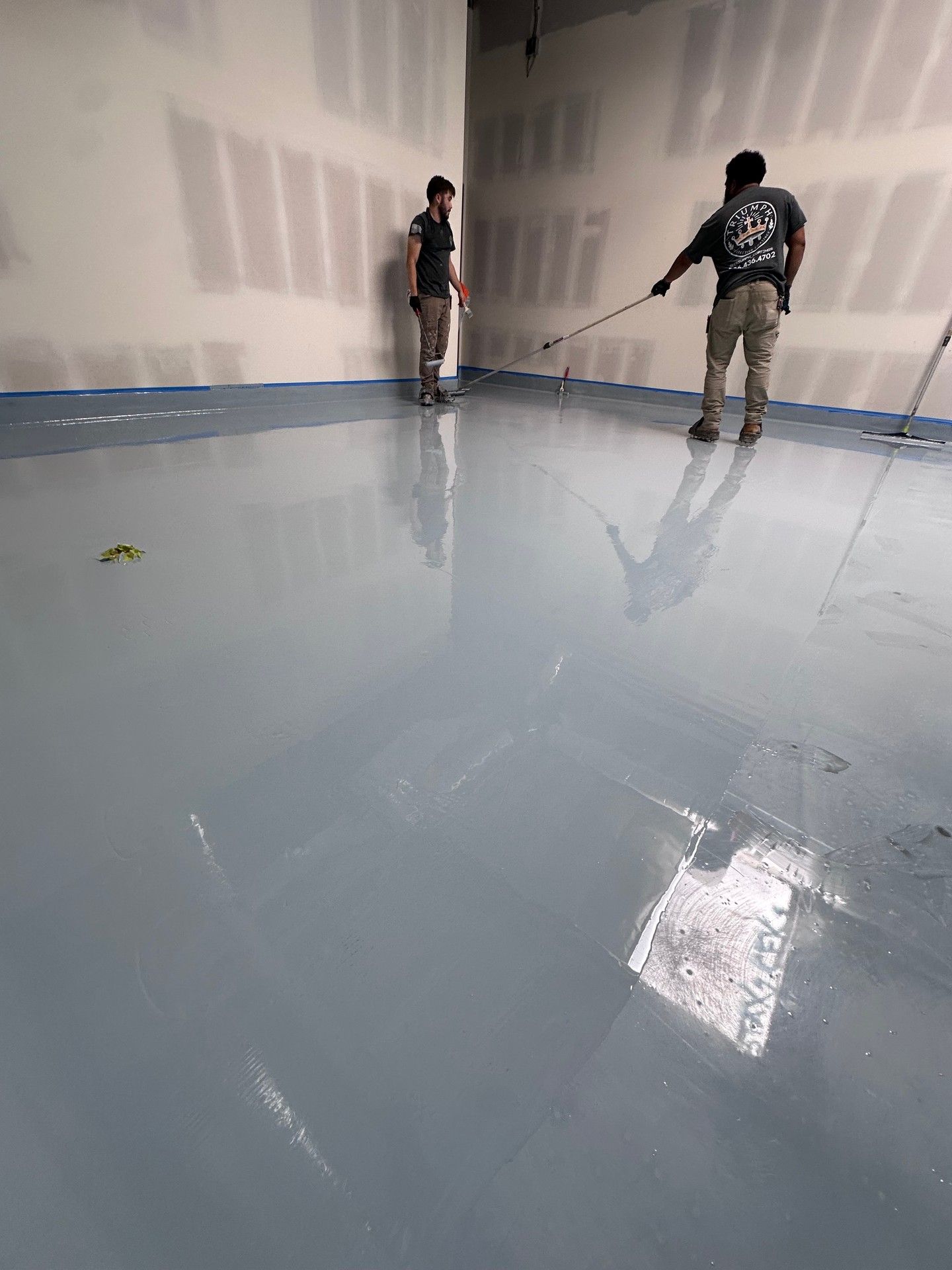 Two people applying blue epoxy floor coating in a large room.