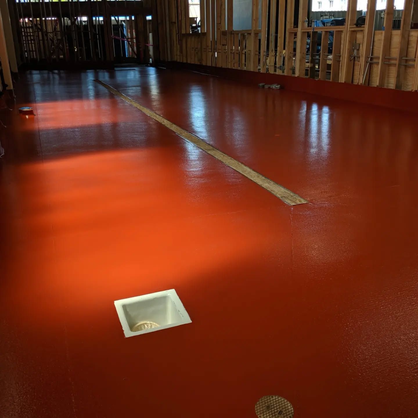Red epoxy floor with a drain and a trench in a room under construction.
