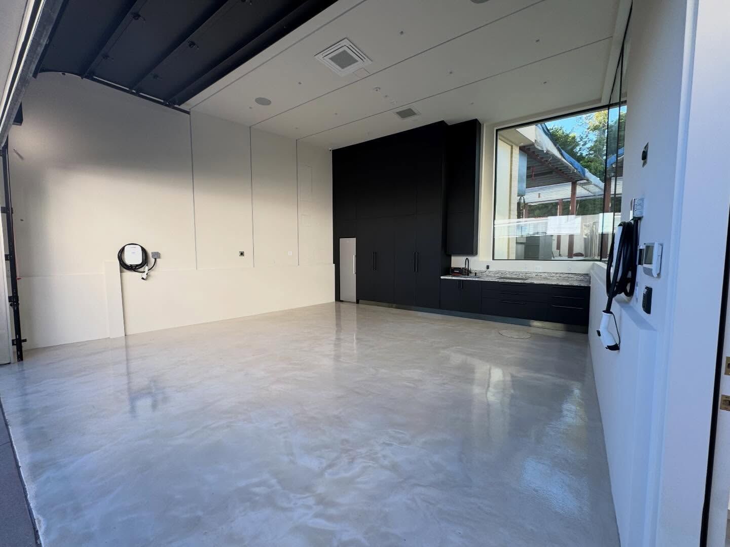 Empty garage with polished concrete floor, black accent wall, and large window; sunlight.