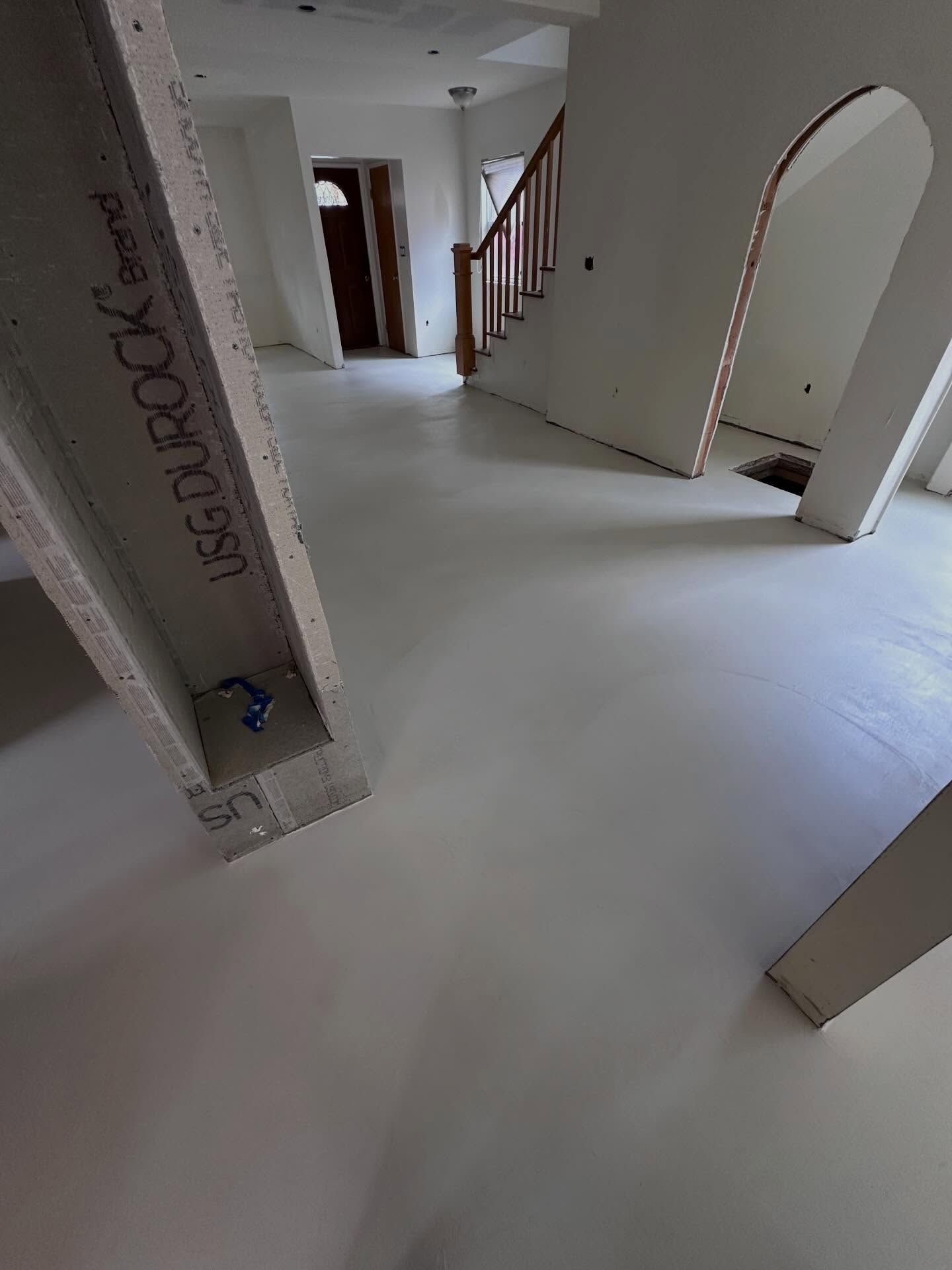 Interior construction site with smooth, light-colored floor; drywall columns, stairs, and doorway.