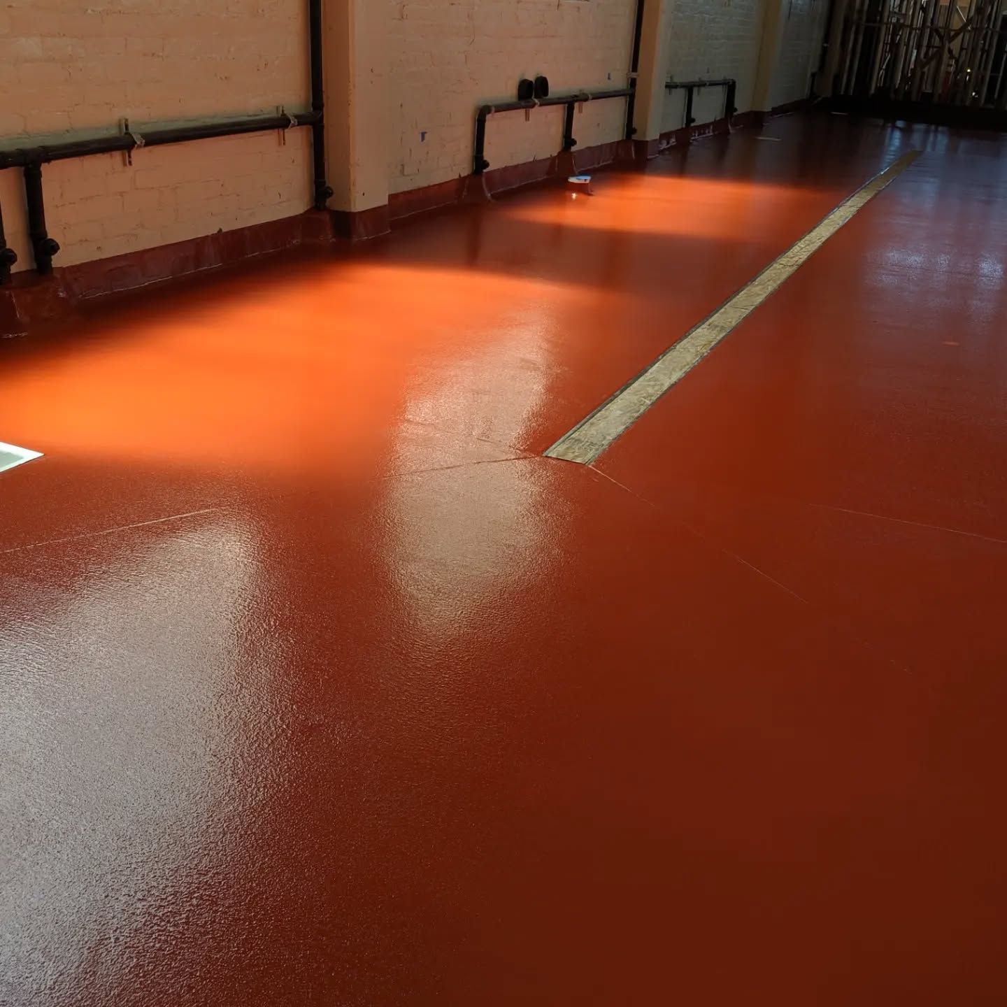 Red, glossy epoxy floor in a room, with a white line and black pipes along walls.