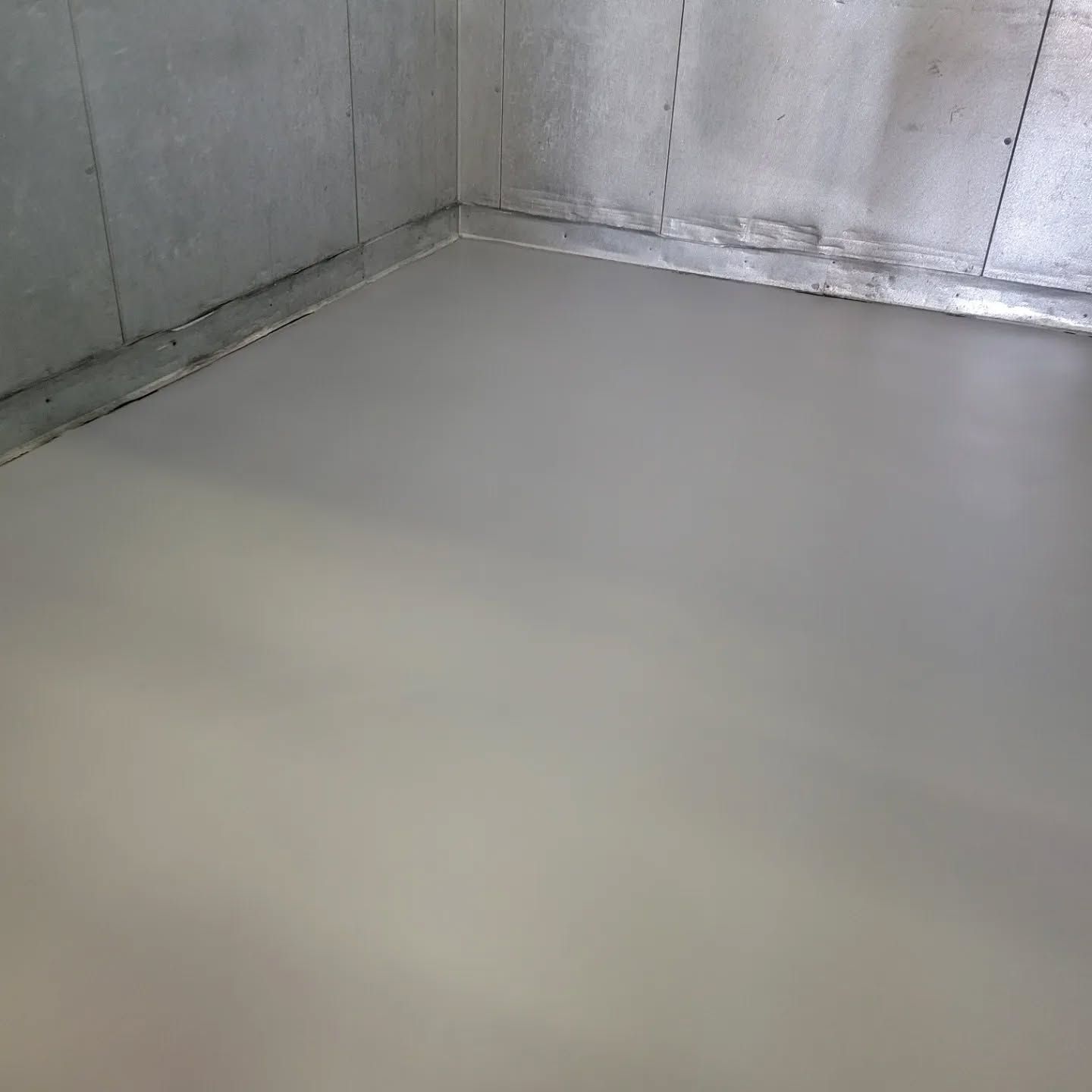 A gray-painted room corner with a smooth floor and concrete walls.