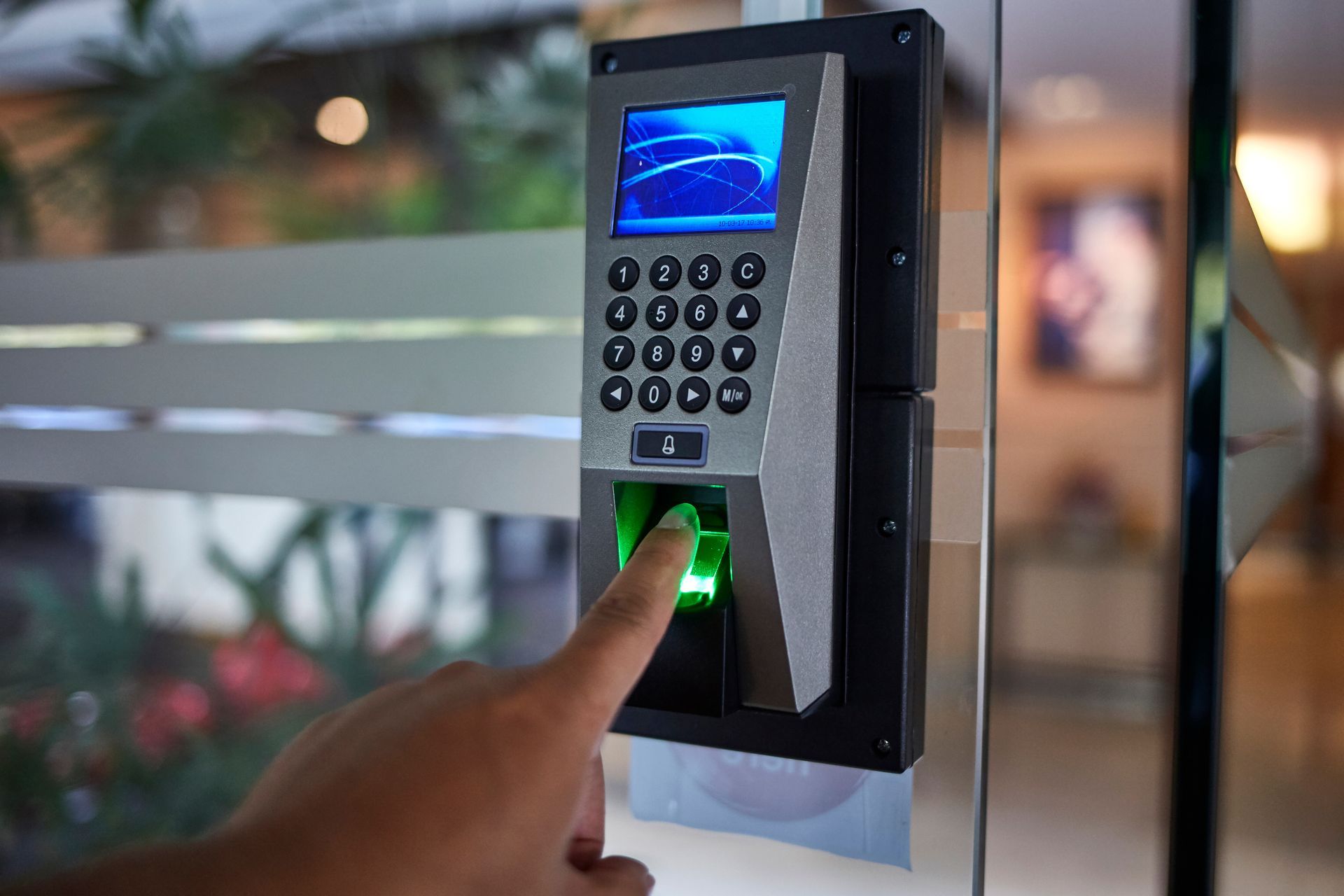 Person using fingerprint scanner on a glass door for access. The scanner is black and gray.