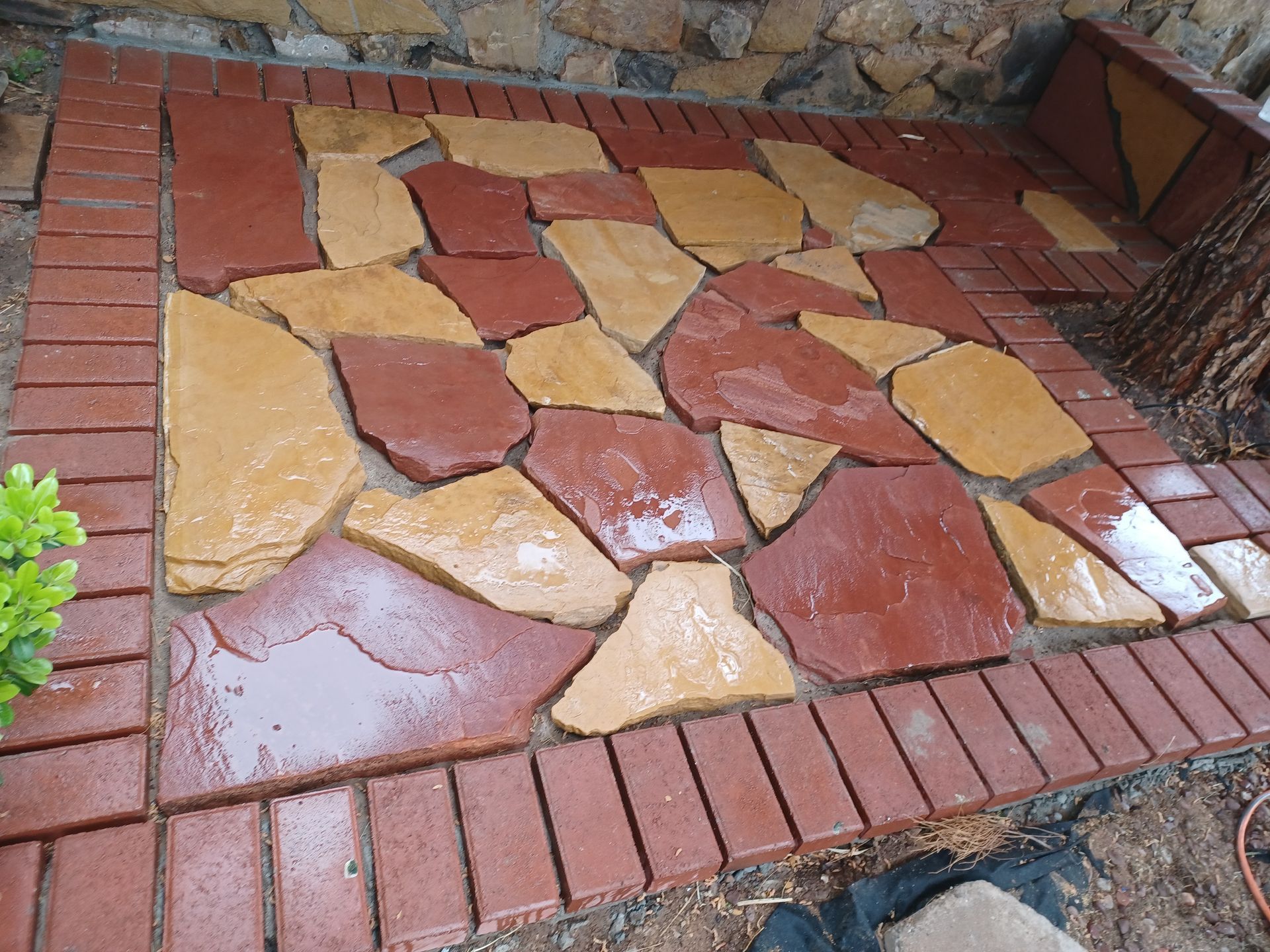 Stone patio with red brick border, featuring irregular reddish-brown and tan stones.