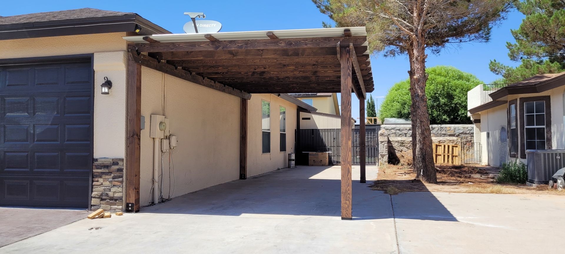 Carport next to a house with a dark garage door, sunny day.