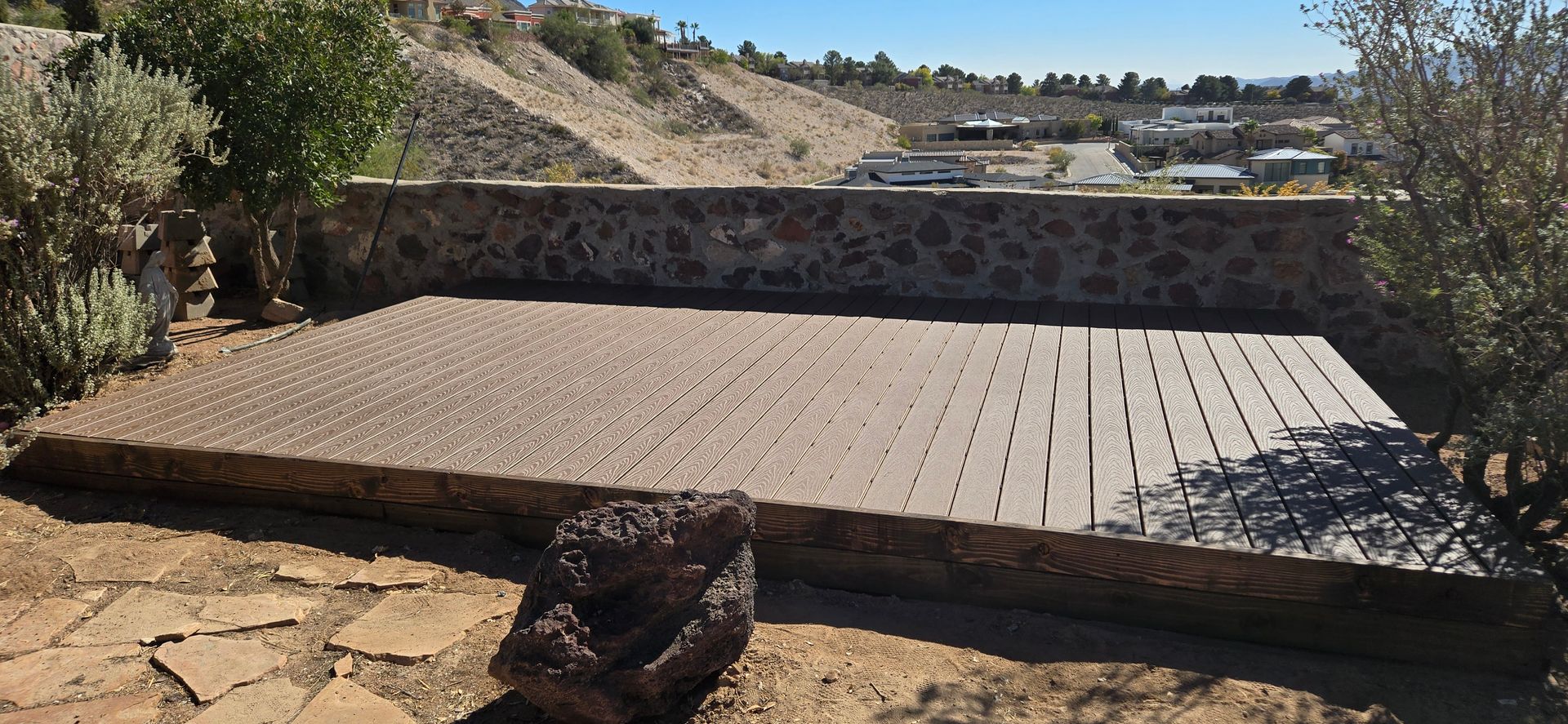 A raised stone patio surrounded by foliage and dry hillside in the background.