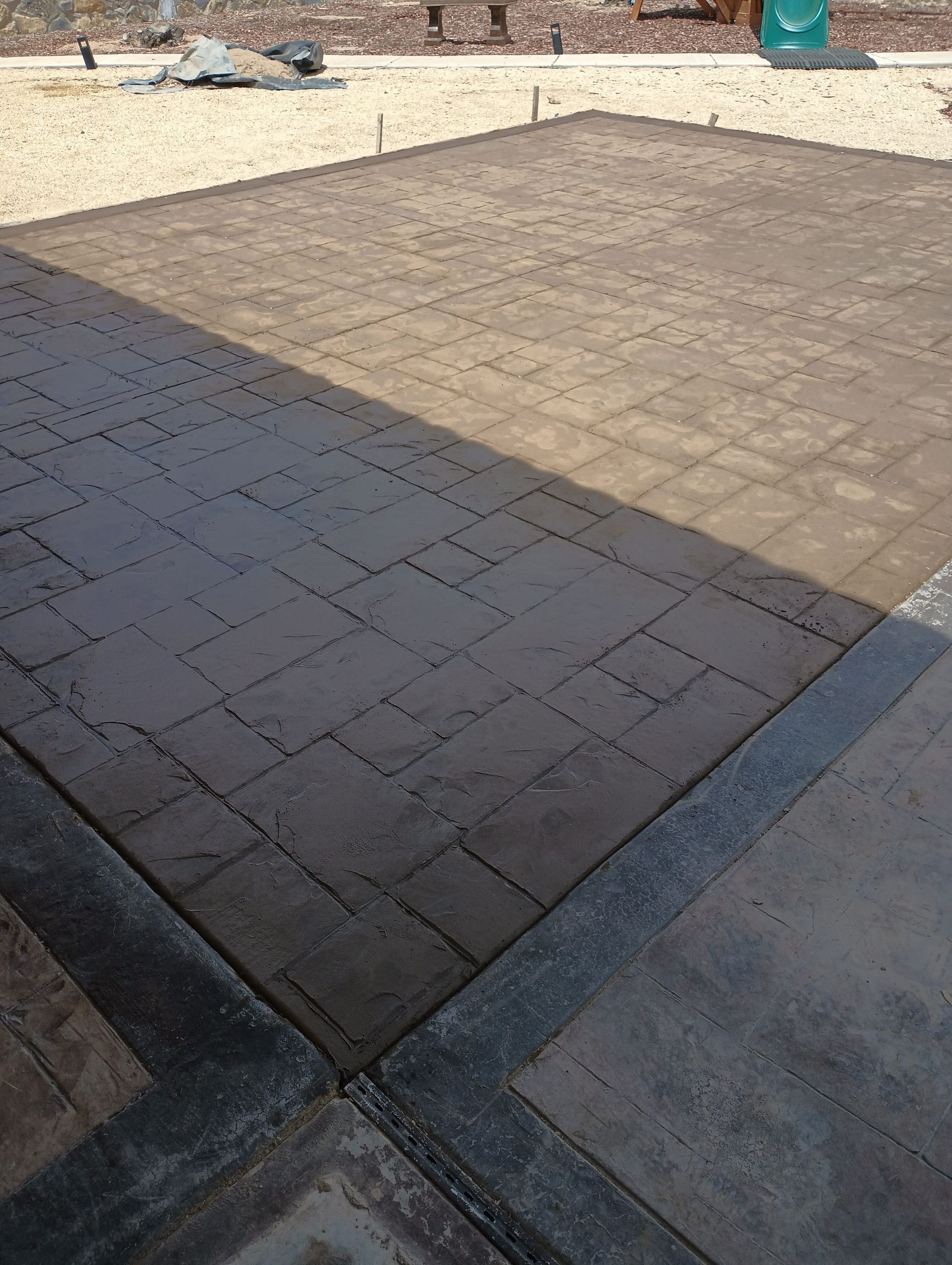 Stamped concrete patio, partially in shadow, with a darker patterned design.
