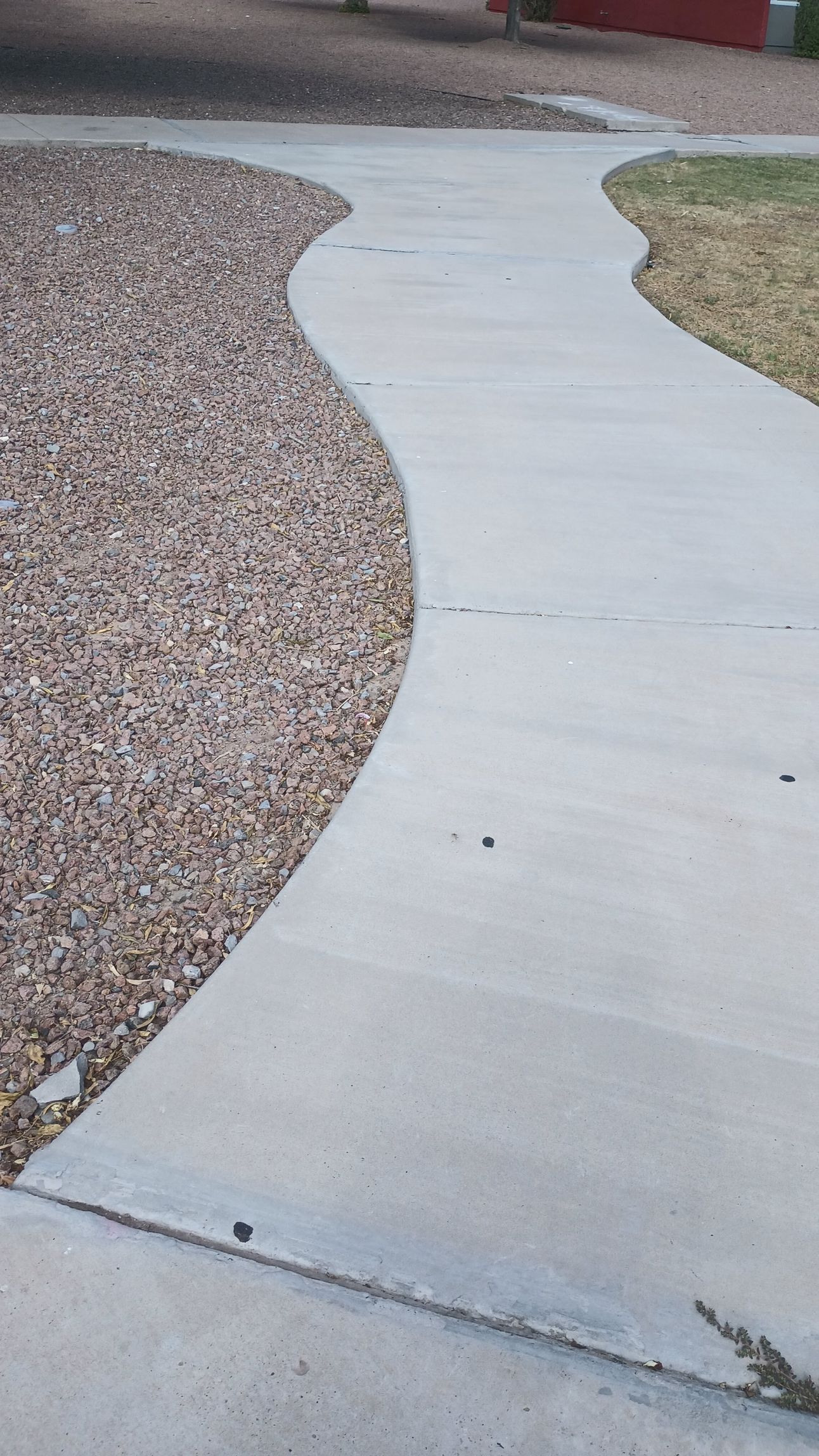 Curving concrete sidewalk next to a bed of brown mulch.