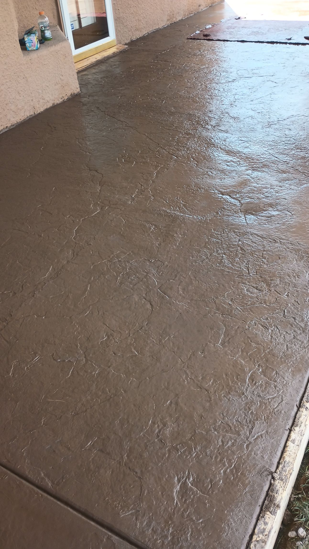 Wet, brown concrete patio along a tan wall; light reflecting off surface.