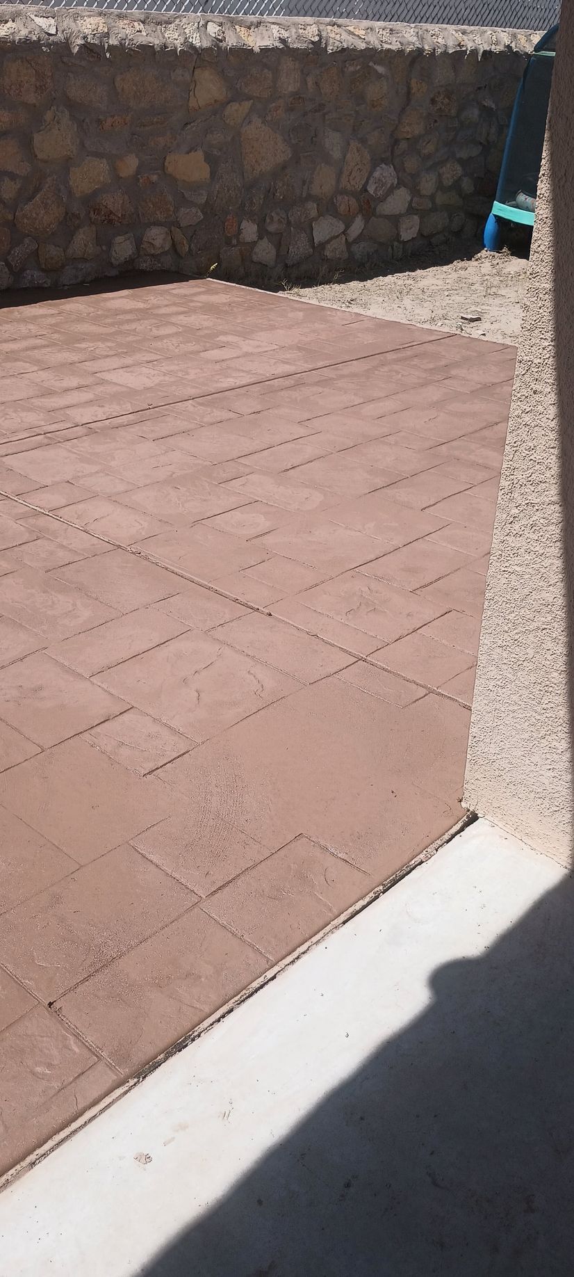 A brick patio next to a stone wall, with a portion of a white structure.