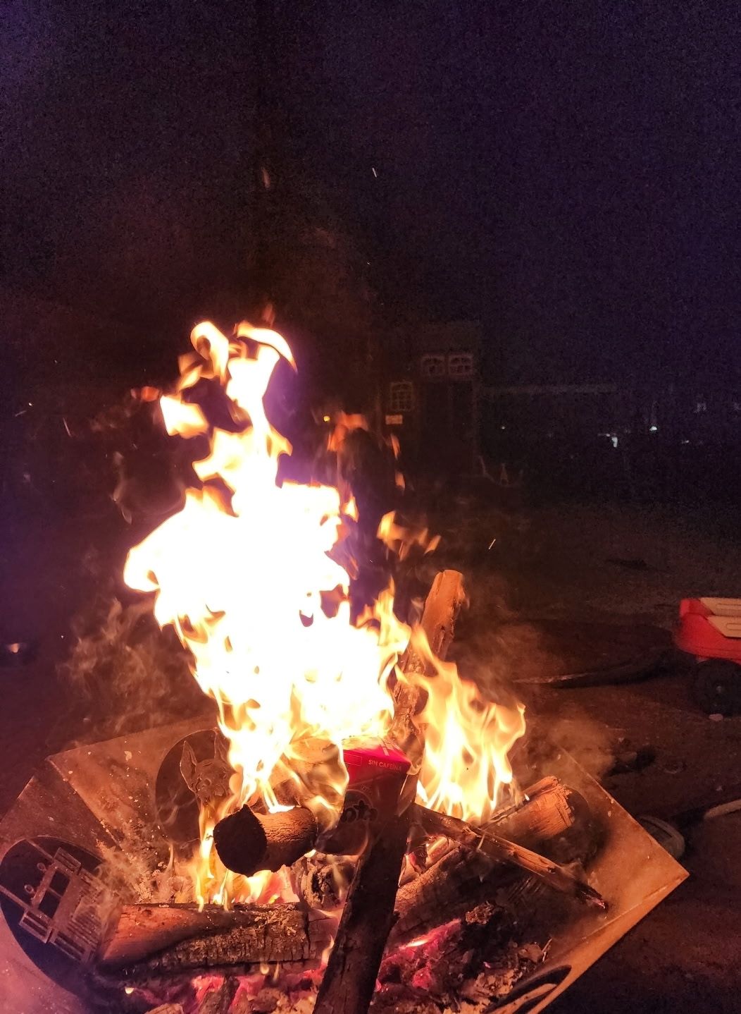 Bonfire at night, flames burning bright in a metal fire pit. Logs are burning below, setting a dark background.