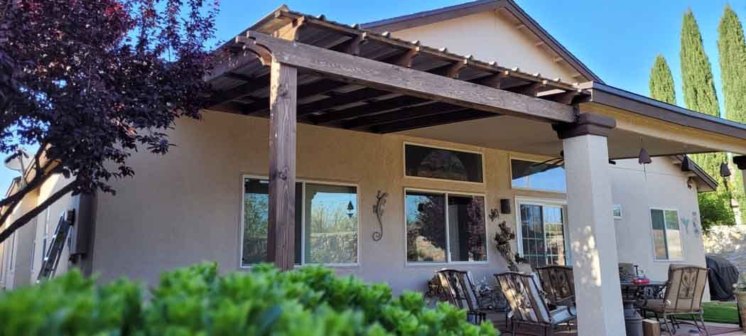 House exterior with a wooden pergola, windows, and green bushes in the foreground.