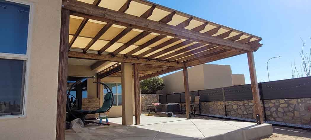 Wooden pergola with canvas shade covers an outdoor patio. Blue sky is visible.