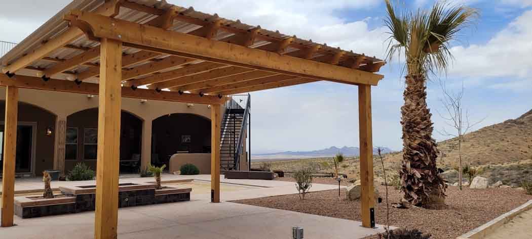 Wooden pergola in front of a house in a desert landscape. Palm tree and distant mountains.