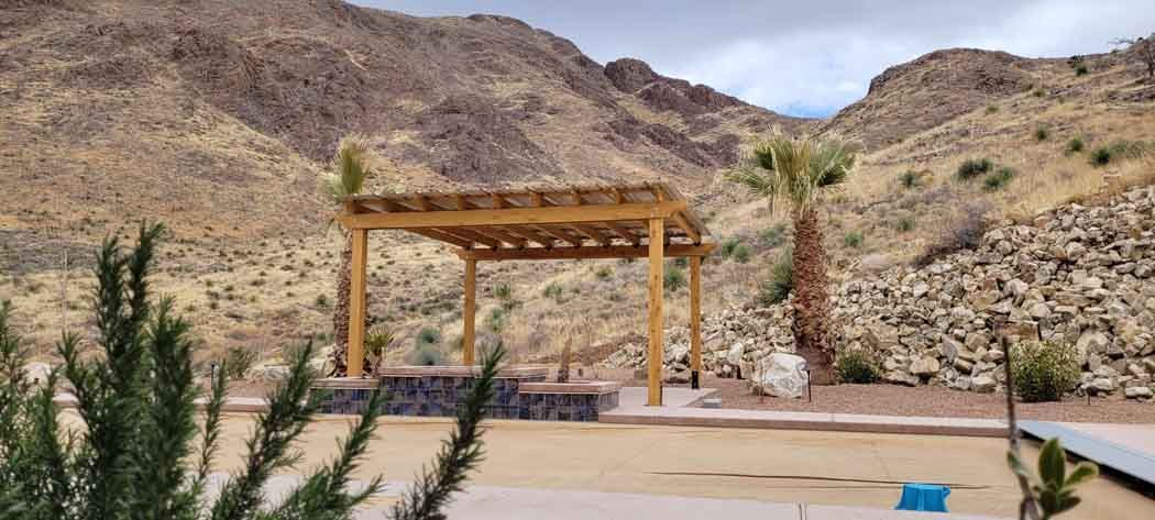 Wooden pergola in a desert landscape with mountains in the background.