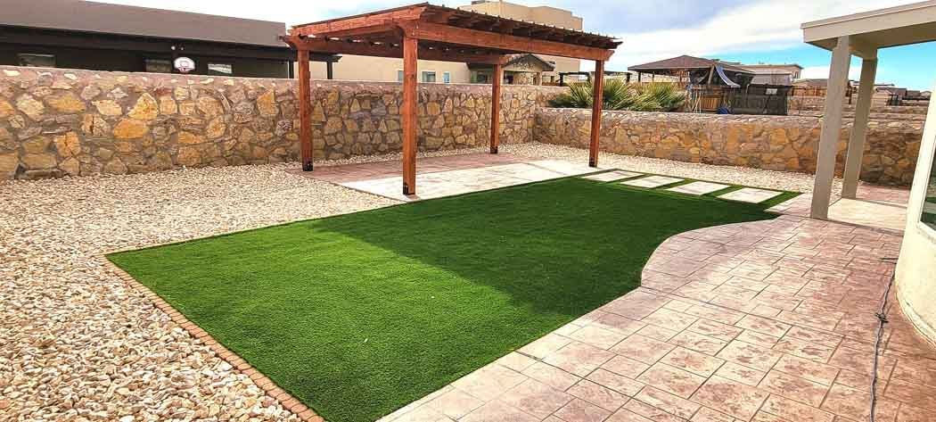 A backyard with a grass area, a wooden pergola, and stone walls.
