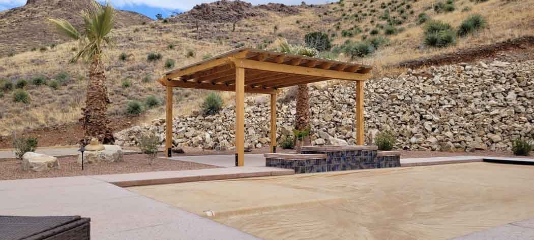 Wooden pergola on a stone base; mountain in the background.