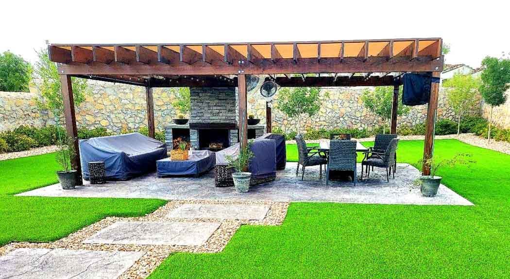 Outdoor patio with pergola, fireplace, seating, and lush green lawn.