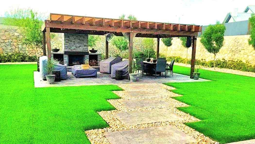 Wooden pergola with fireplace, seating area, stone pathway, and green lawn.