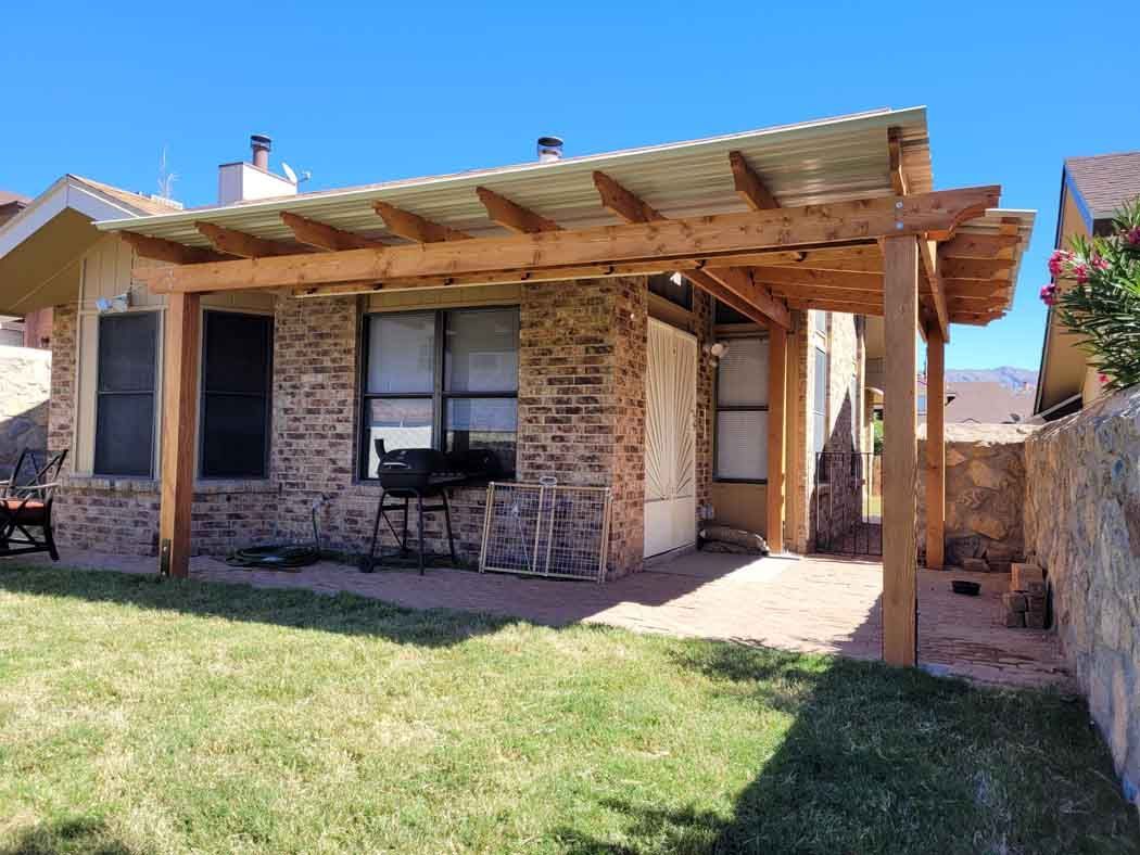 Backyard with a brick home, wooden pergola, green grass, and a stone wall.