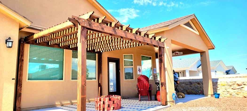 Exterior of a house with a wooden pergola, a red chair, and a clear blue sky.