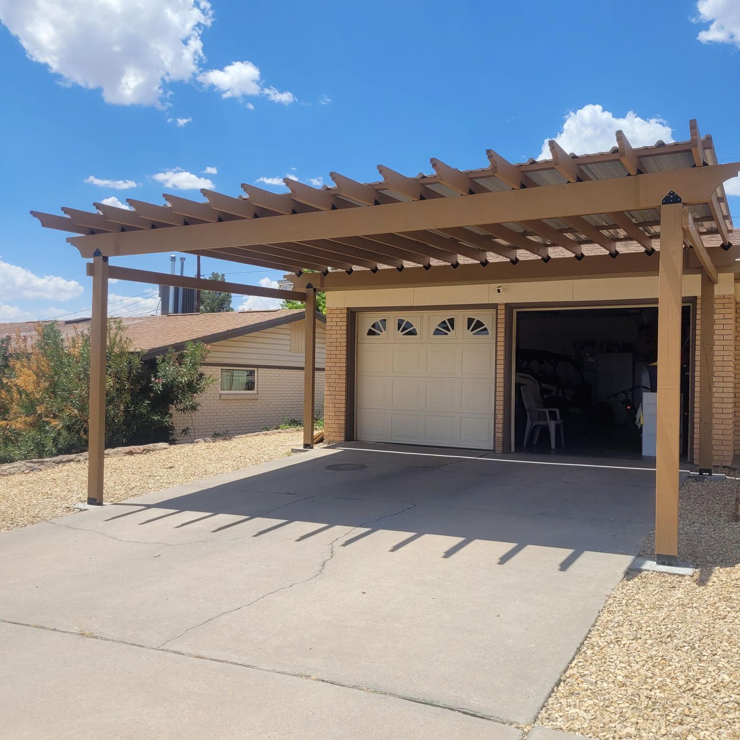 Brown pergola covers a garage and driveway on a sunny day.