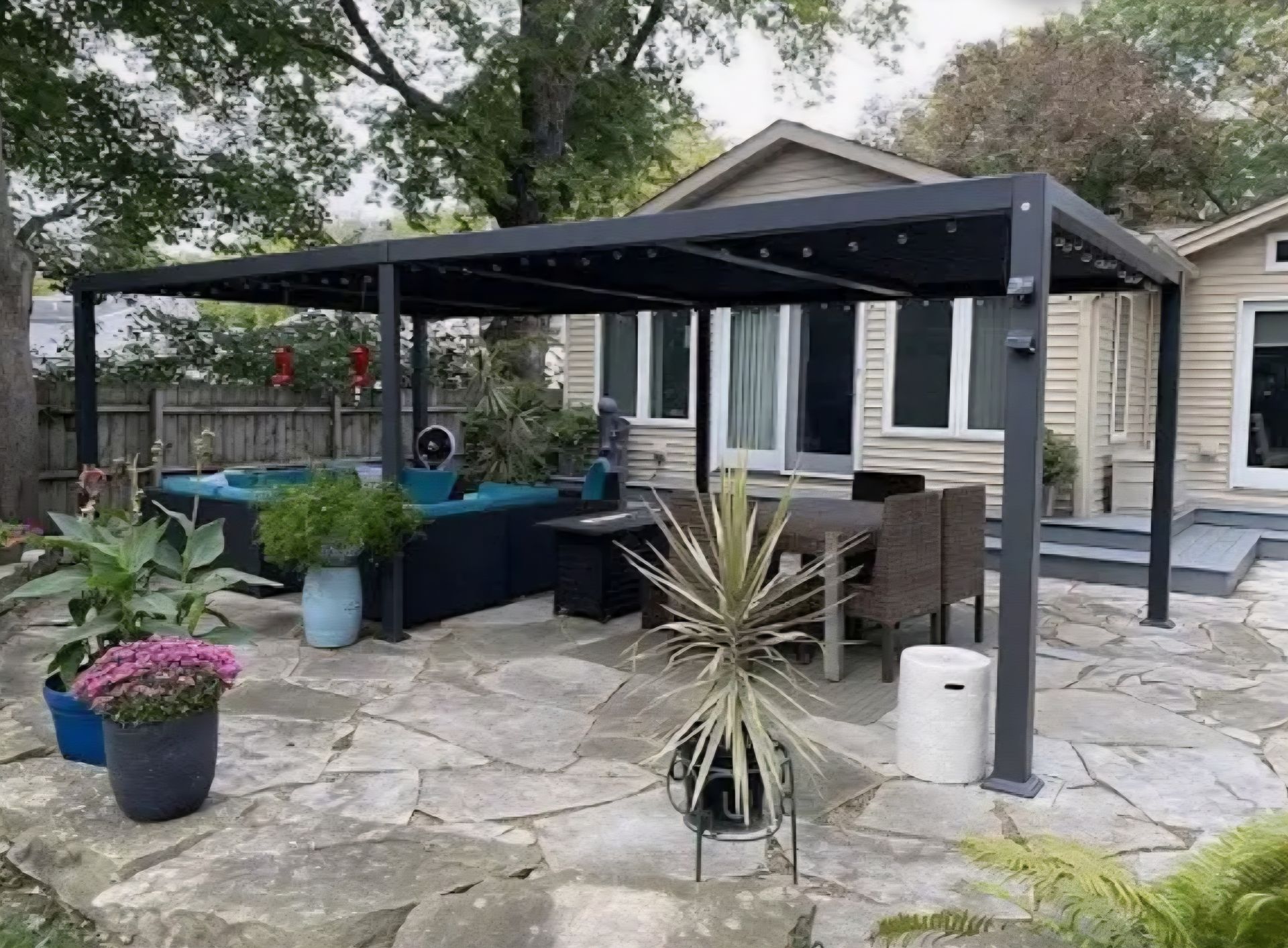 Black pergola over outdoor patio with seating and plants.