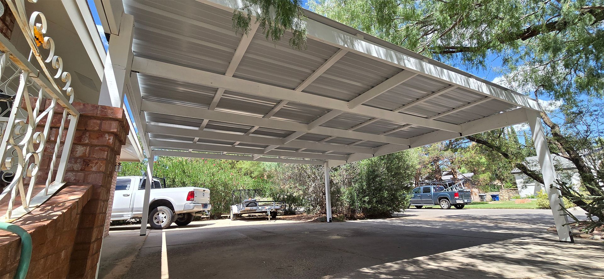 A car is parked under a white carport. Other vehicles and trees are in the background.