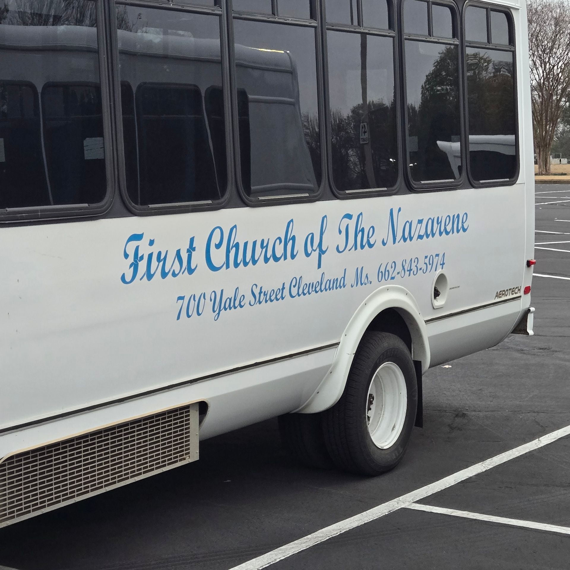 Side view of a white church shuttle bus with blue text reading 