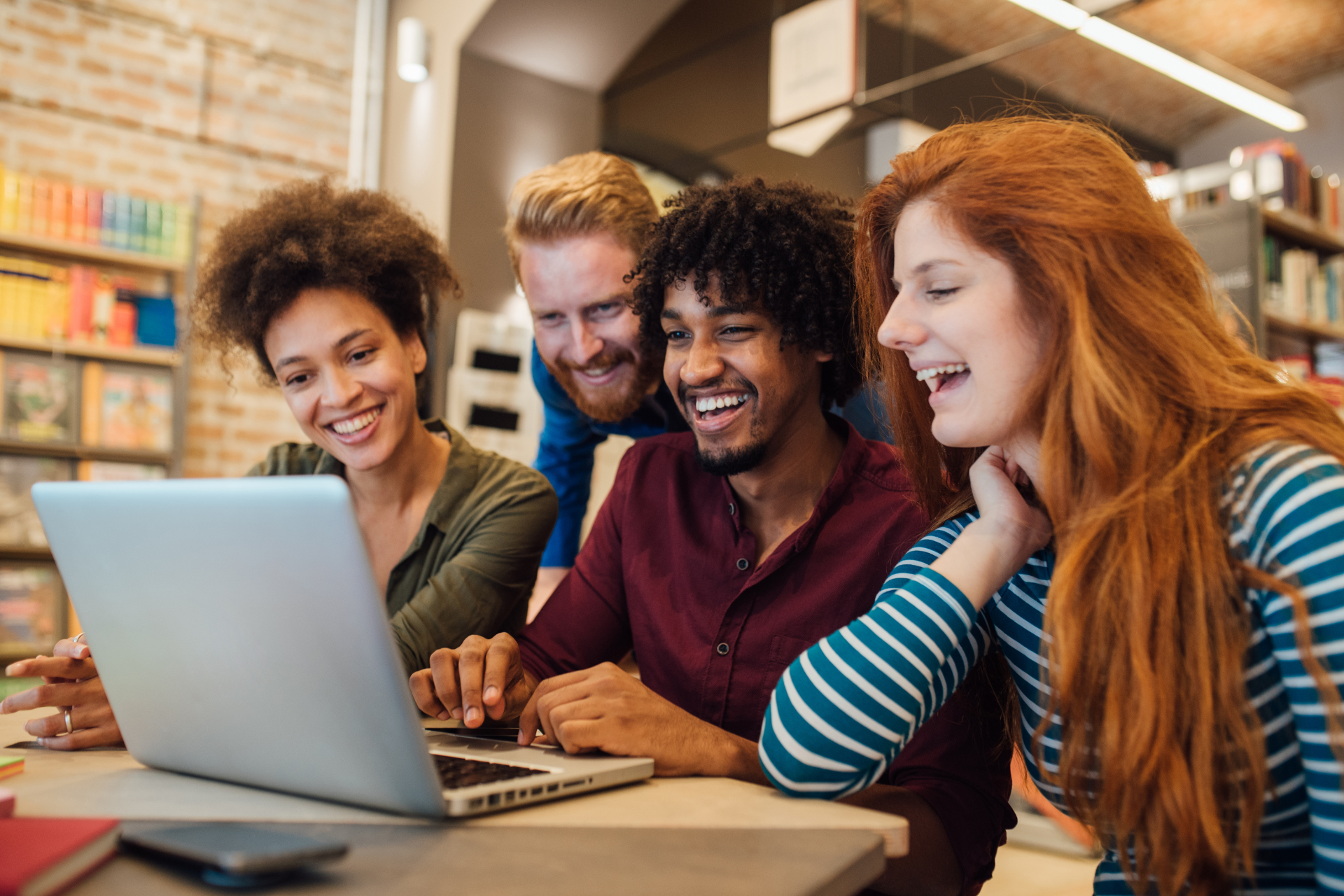 A group of young people are sitting at a table looking at a laptop computer.