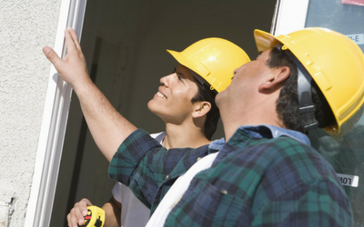 Two construction workers, wearing yellow hard hats, inspecting a doorway. One points up.