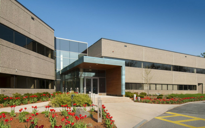 Modern two-story building with a glass entrance, surrounded by red tulips and a paved walkway.