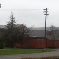 A brick wall surrounds a large building with a tall power pole in front of it. Overcast sky.